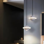 Two grey Clérachic planet pendants lit at different heights in a dark hallway beside a wall of black slats, with a warm glow below.