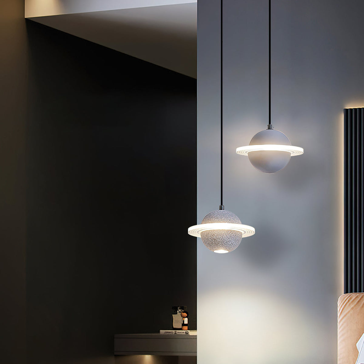 Two grey Clérachic planet pendants lit at different heights in a dark hallway beside a wall of black slats, with a warm glow below.