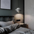 This Clérachic pendant with a grey speckled sphere and ring hangs beside a bed with rumpled grey bedding and a dark green wall.