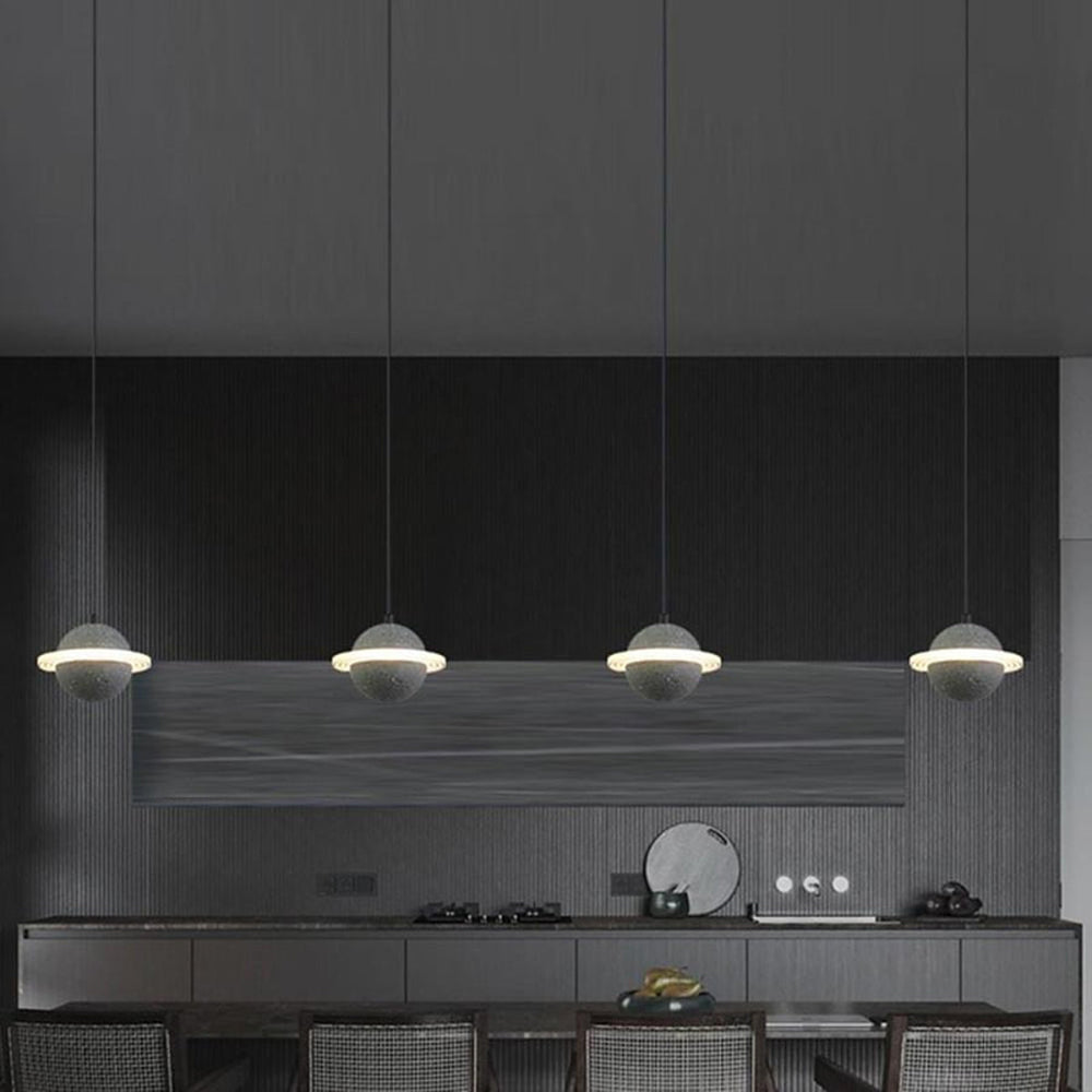 Row of four grey Clérachic planet pendants hanging over a dark kitchen worktop, with a glowing ring around each sphere.
