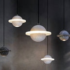 Clérachic planet pendants in grey, black and white at different heights against a dark wall, with their rings and spotlights glowing.