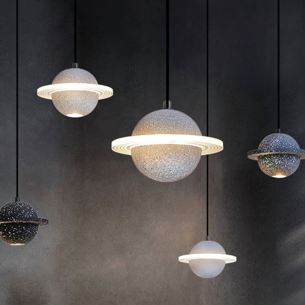 Clérachic planet pendants in grey, black and white at different heights against a dark wall, with their rings and spotlights glowing.