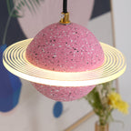 Close view of the sand pink Clérachic pendant, with a ridged glowing ring around the speckled sphere and a blue vase behind.