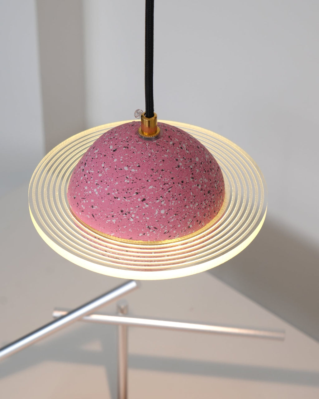 Underside view of the sand pink Clérachic pendant, with the ridged ring glowing above a metal sculpture on the desk below.