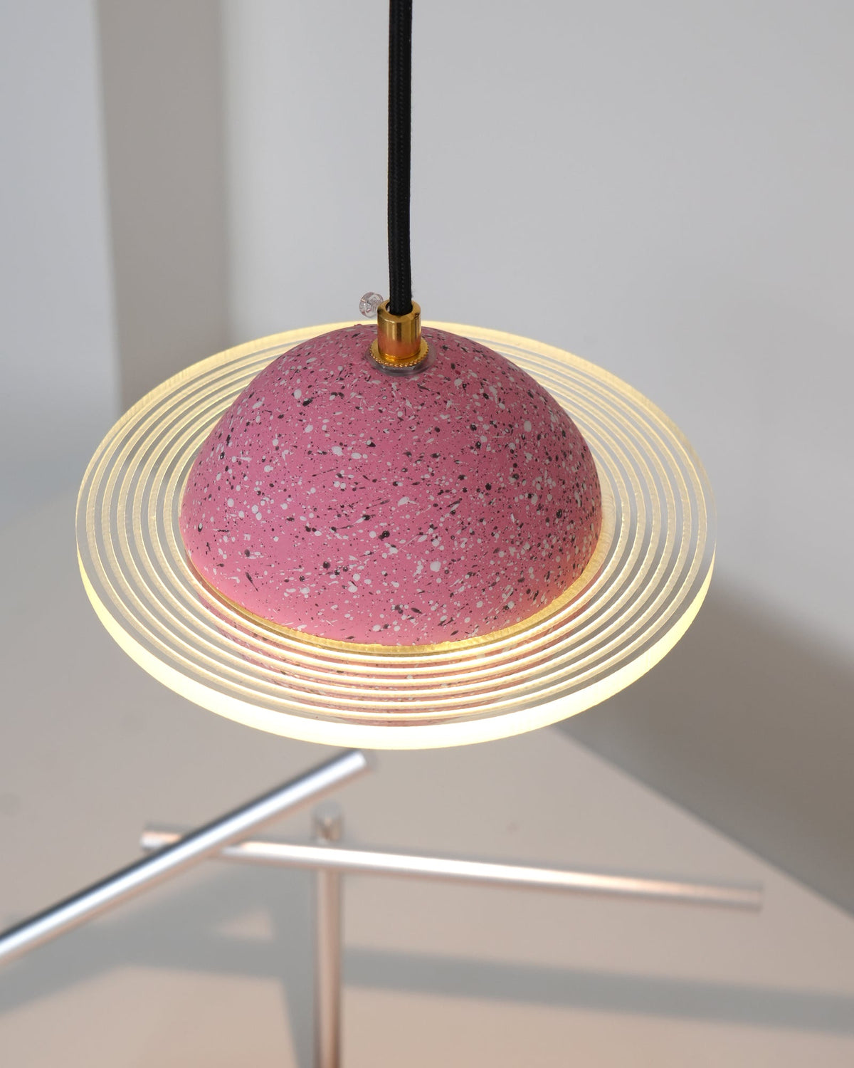 Underside view of the sand pink Clérachic pendant, with the ridged ring glowing above a metal sculpture on the desk below.