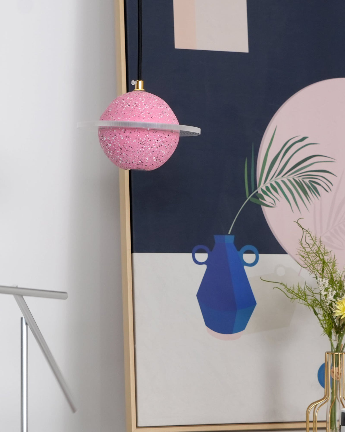 A sand pink Clérachic pendant with a flat, unlit ring hangs beside a tall framed print with a blue vase and a pink circle.