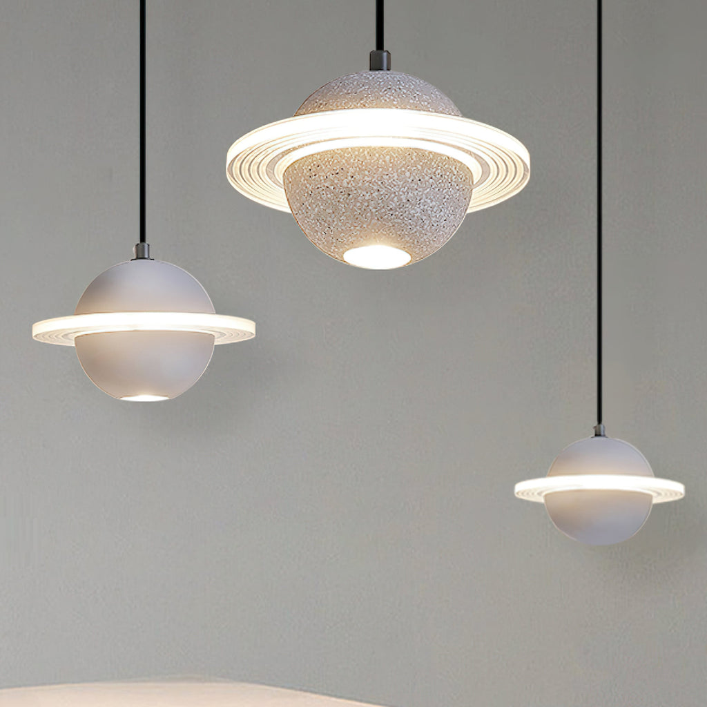 Three Clérachic planet pendants in grey and white hang at different heights against a grey wall, with glowing rings and downlights.