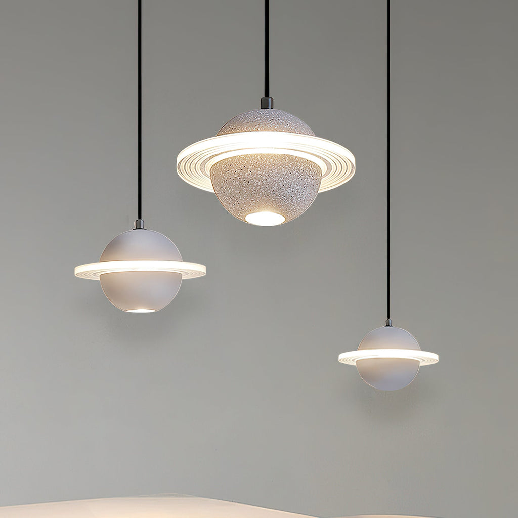 Three white and grey Clérachic pendants with glowing rings, hanging at staggered heights against a soft green-grey wall.