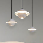Three white and grey Clérachic pendants with glowing rings, hanging at staggered heights against a soft green-grey wall.