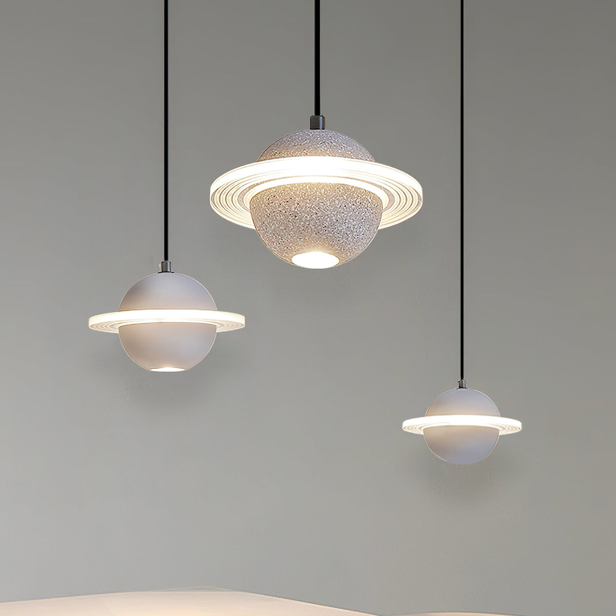 Three white and grey Clérachic pendants with glowing rings, hanging at staggered heights against a soft green-grey wall.