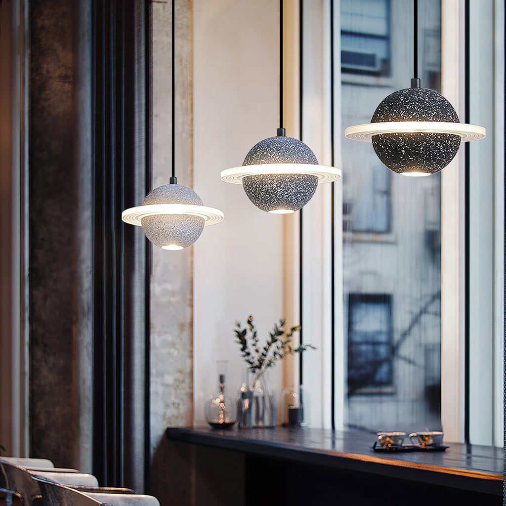 Three Clérachic planet pendants, from pale grey to black, hang beside a tall window onto a city street, above a dark counter.