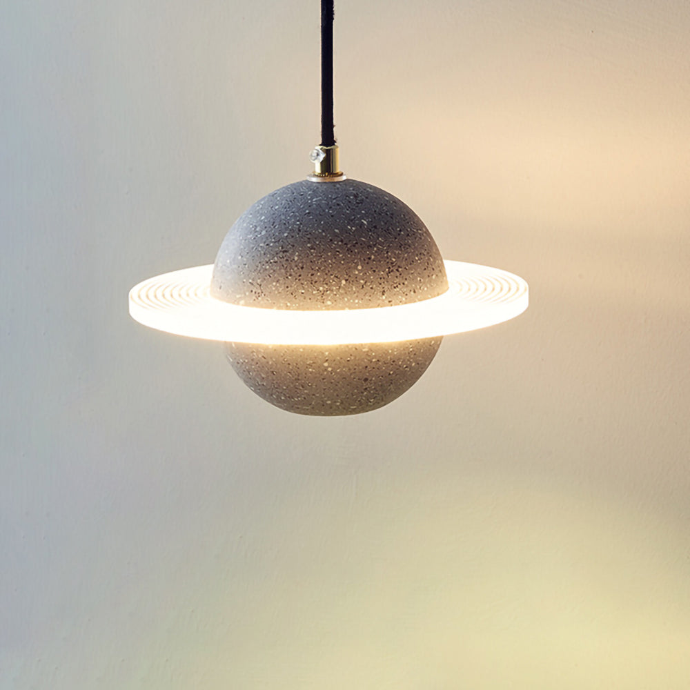 Sand black speckled Clérachic pendant with a bright glowing ring, hanging on a fine cord against a warm cream wall.