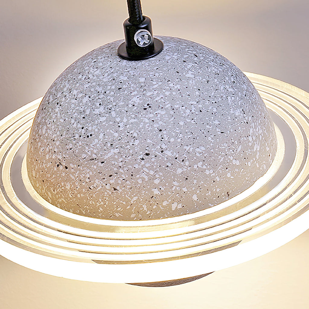 Close view of a pale grey terrazzo-style sphere and the glowing ridged ring of this Clérachic pendant, with a black cord at the top.