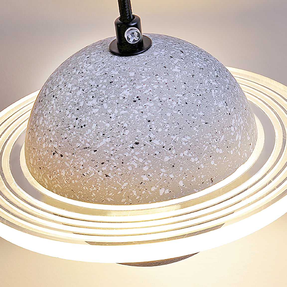Close view of a pale grey terrazzo-style sphere and the glowing ridged ring of this Clérachic pendant, with a black cord at the top.