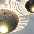 Close view of the lit bulb under a grey speckled sphere and its ridged ring on this Clérachic pendant, with a second pendant behind.
