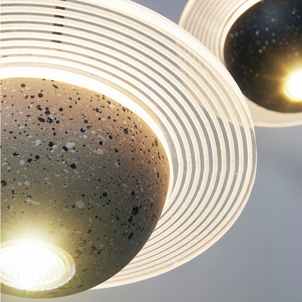 Close view of the lit bulb under a grey speckled sphere and its ridged ring on this Clérachic pendant, with a second pendant behind.