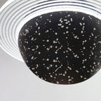 Close view of the underside of a sand black Clérachic pendant, with white flecks on the sphere and a clear ridged ring above.