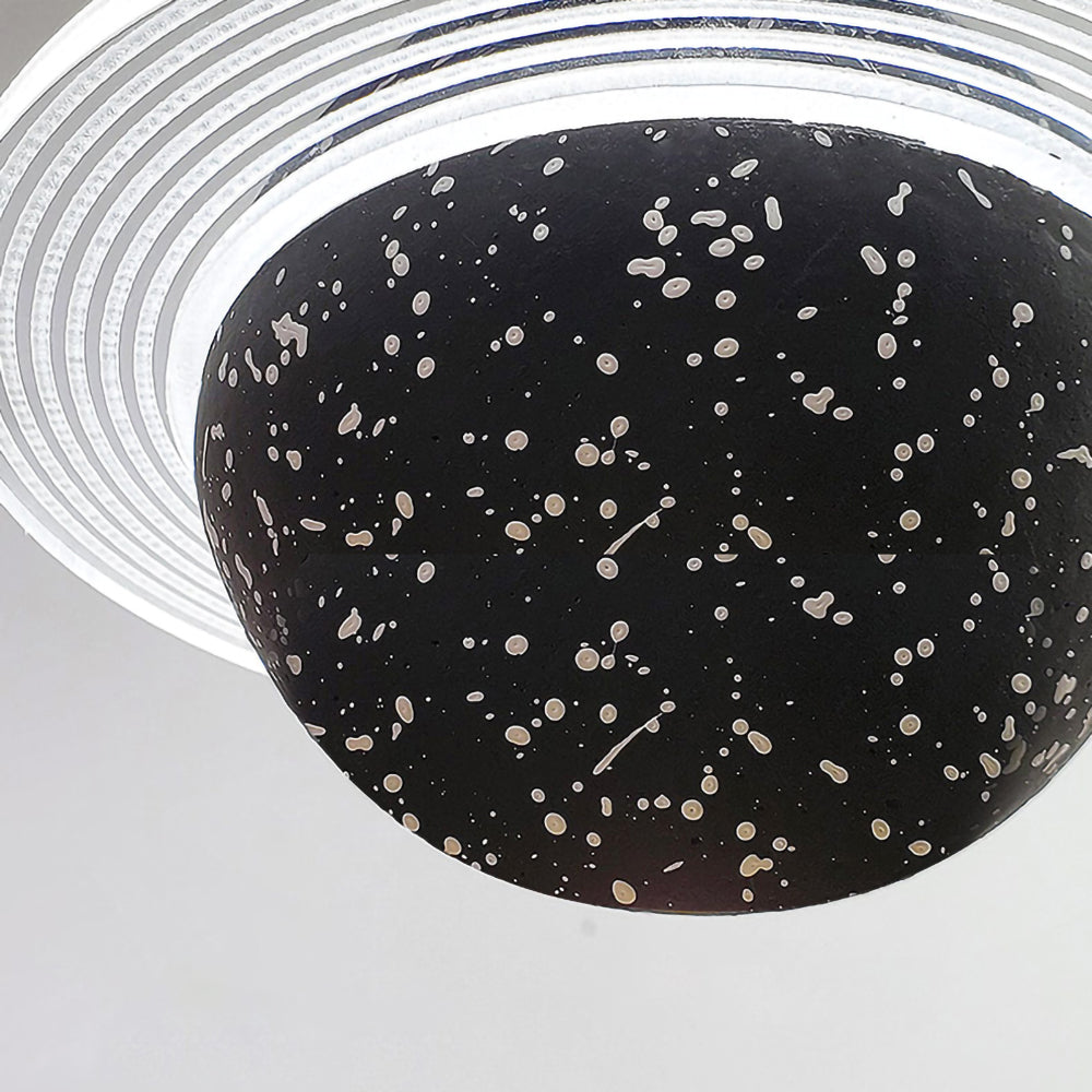 Close view of the underside of a sand black Clérachic pendant, with white flecks on the sphere and a clear ridged ring above.