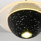 Looking up at a sand black Clérachic pendant, with a lit bulb at the base of the speckled sphere and a glowing ring around it.