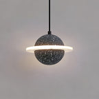 A sand black Clérachic pendant with a lit ring, hanging on a black cord against a warm grey wall.