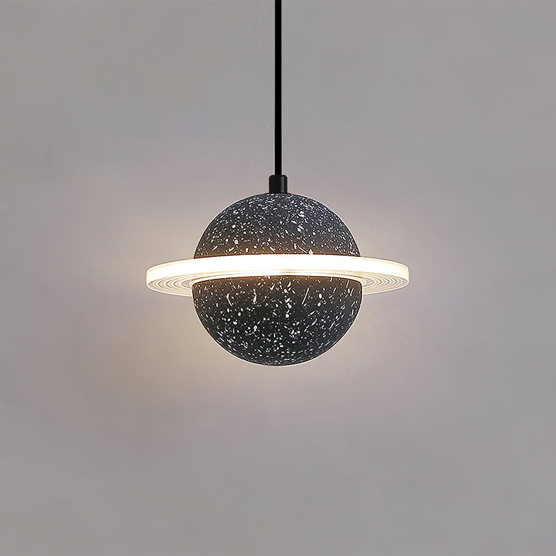 A sand black Clérachic pendant with a lit ring, hanging on a black cord against a warm grey wall.