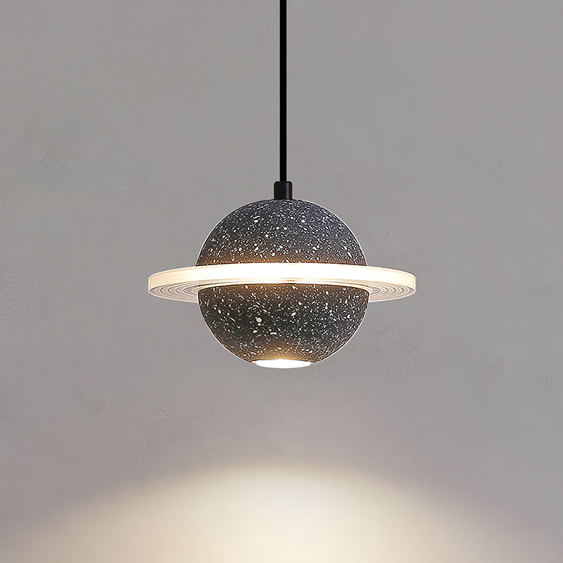 Lit sand black Clérachic pendant with a glowing ring and a spot of light below, against a warm grey wall.