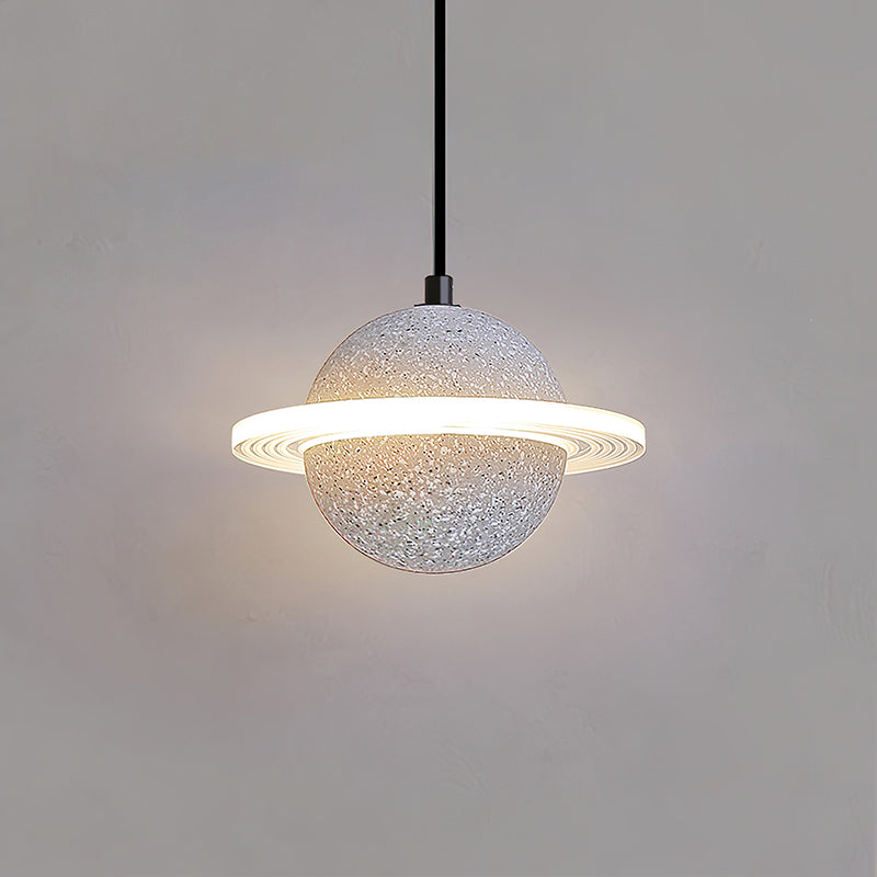 Pale speckled Clérachic pendant with a glowing ring and a soft halo on a grey wall, hanging on a black cord.
