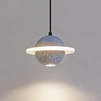 Lit grey blue Clérachic pendant with a bright ring and a pool of warm light below it on a grey wall.