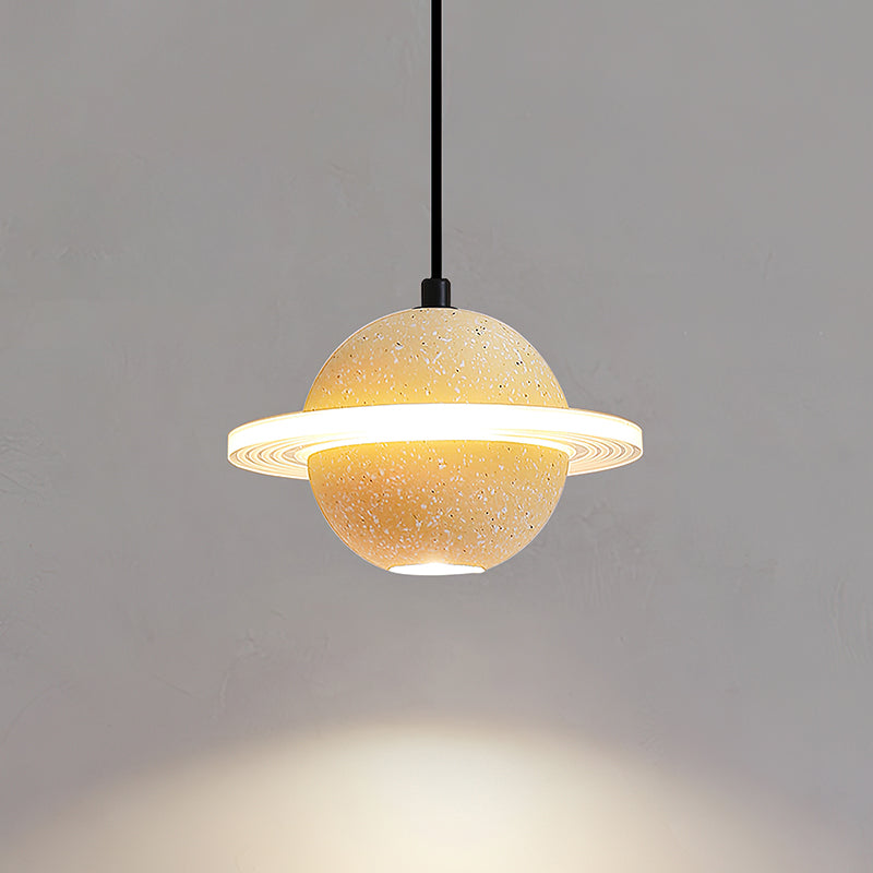 A sand yellow Clérachic pendant with a lit ring casts a warm pool of light downwards on a grey wall.