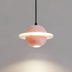 Lit Clérachic pendant with a coral-pink sphere and a ridged ring, throwing a warm circle of light on the wall below.