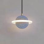 Grey blue speckled Clérachic pendant with a brass cord top and a glowing ring, hanging against a grey wall.