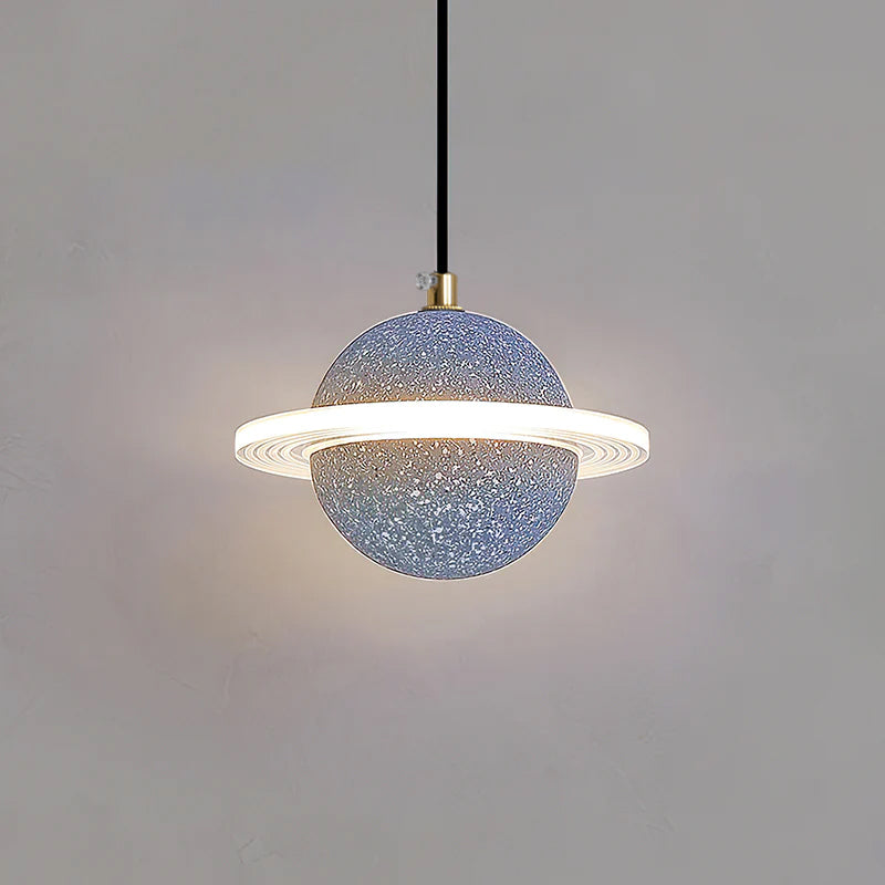 Grey blue speckled Clérachic pendant with a brass cord top and a glowing ring, hanging against a grey wall.