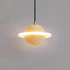 A Clérachic pendant with a sand yellow sphere, brass cord top and bright ring, glowing against a grey wall.