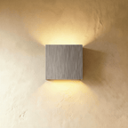 This Clérachic square wall lamp in brushed silver casts warm up-and-down light on a plain plaster wall.