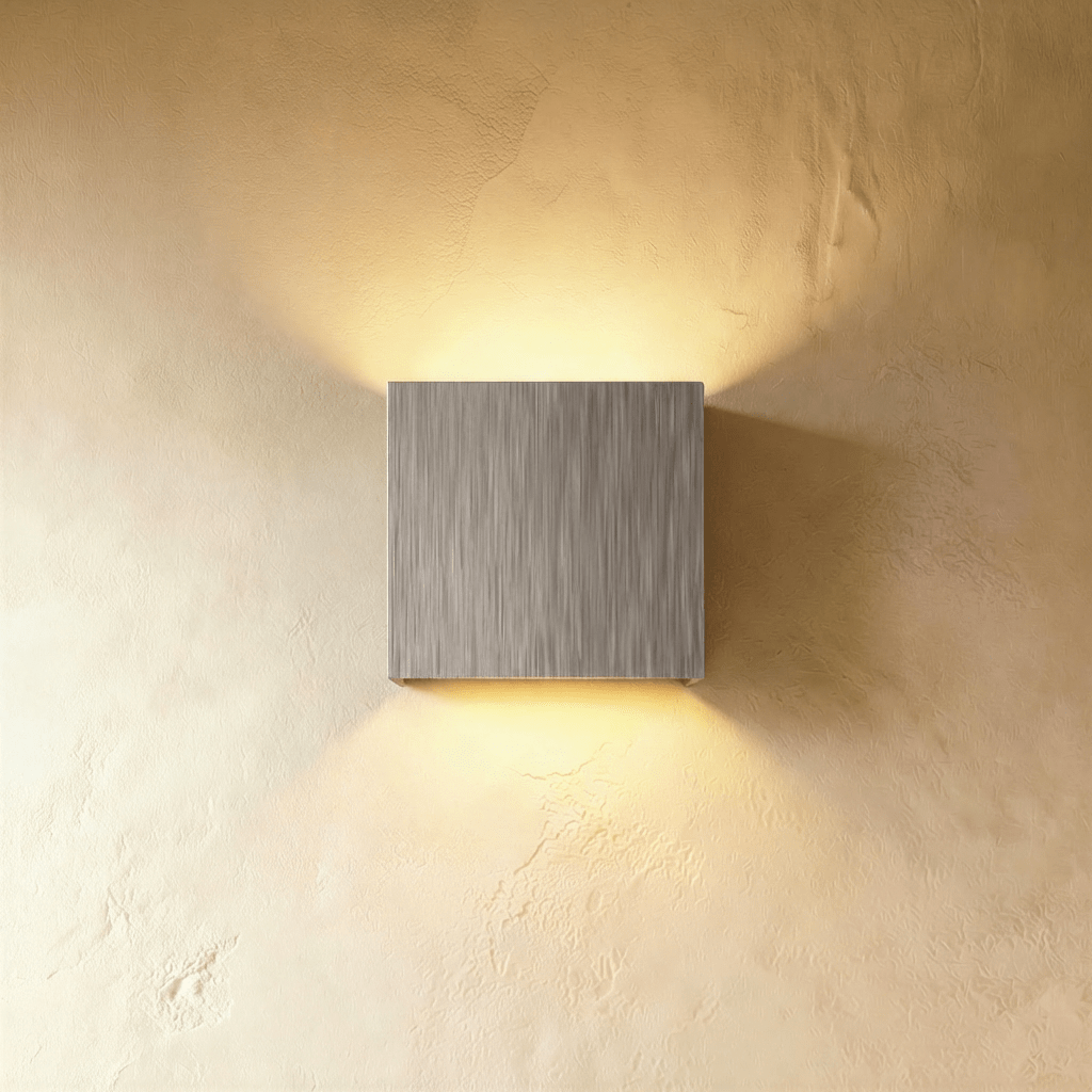 This Clérachic square wall lamp in brushed silver casts warm up-and-down light on a plain plaster wall.