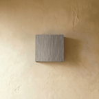 Clérachic's brushed silver square wall lamp sits unlit against a warm plaster wall in this front view.