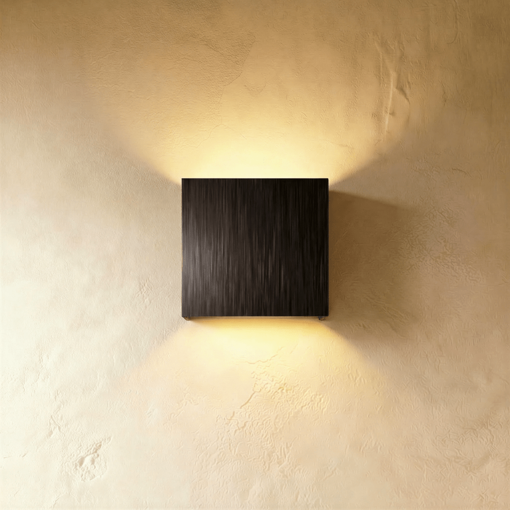 This Clérachic square wall lamp in a brushed black finish glows warmly up and down a plaster wall.