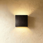 This Clérachic square wall lamp in a brushed black finish glows warmly up and down a plaster wall.