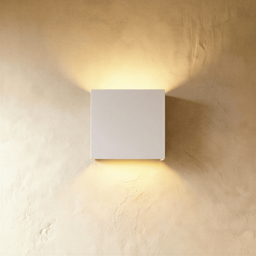 This Clérachic square wall lamp in matte white finish casts warm light up and down a plaster wall.