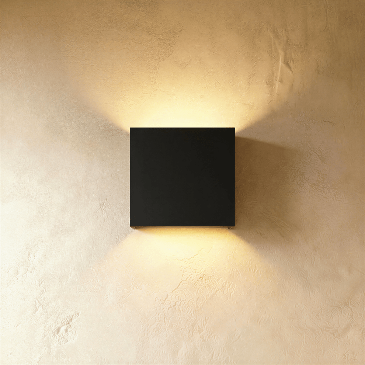 This Clérachic square wall lamp in matte black finish casts warm up-and-down light on a plain wall.