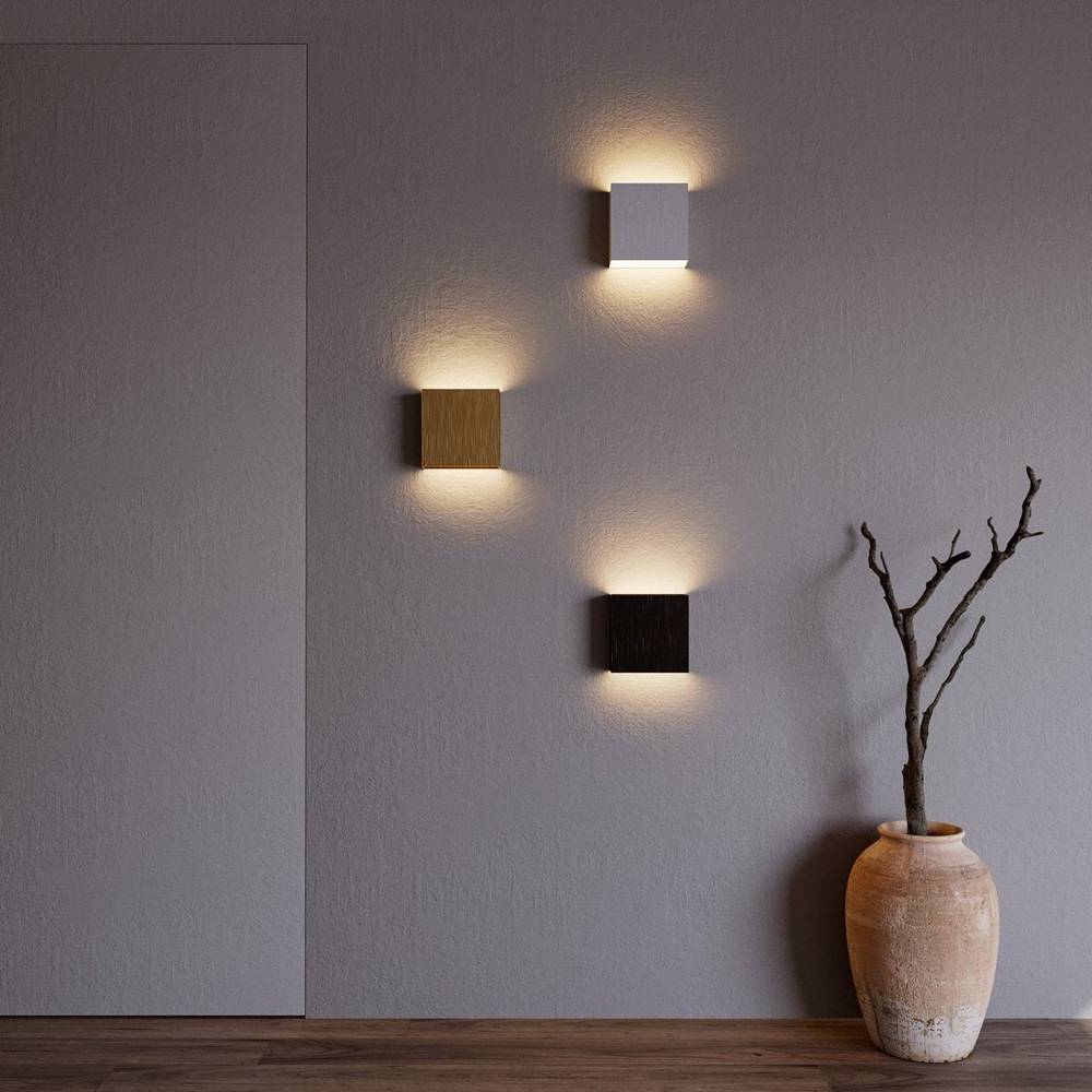 Three Clérachic square wall lamps in silver, gold and black light a gray wall beside a terracotta vase.