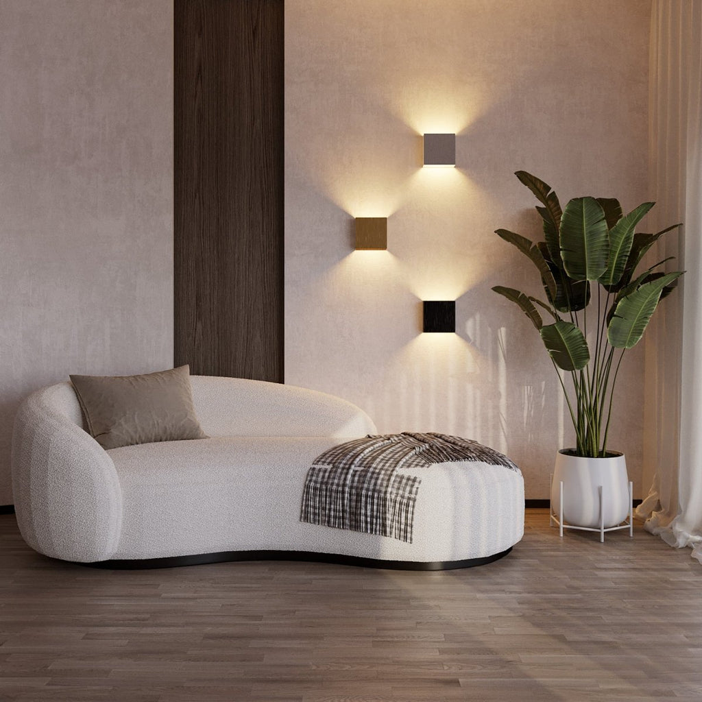 Three Clérachic square wall lamps glow above a curved boucle sofa and potted plant in this living room.