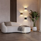 Three Clérachic square wall lamps glow above a curved boucle sofa and potted plant in this living room.