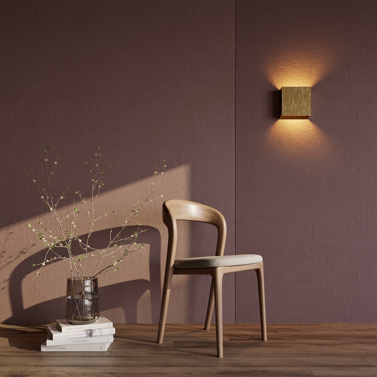 A brushed gold Clérachic square wall lamp glows above a wooden chair against a plum-toned wall.