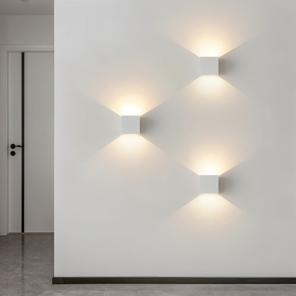 Three matte white Clérachic square wall lamps cast a diagonal pattern of warm light in a hallway.