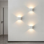 Three matte white Clérachic square wall lamps cast a diagonal pattern of warm light in a hallway.