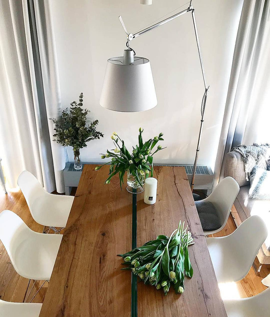 Clérachic floor lamp arm reaches over a long oak dining table with white chairs and a bunch of fresh tulips.