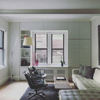 Clérachic arc floor lamp in a pale living room with a window, black leather chairs and a quilted grey sofa.
