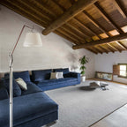 Clérachic floor lamp rising beside a navy corner sofa in a loft living room with exposed wooden roof beams.