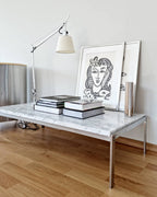 Clérachic floor lamp leaning in over a marble coffee table stacked with books and a framed line drawing.